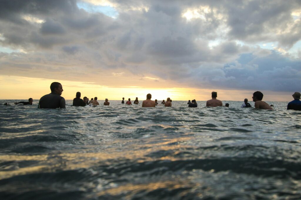 Group of people enjoying a tranquil sunset swim in the ocean under a cloudy sky.